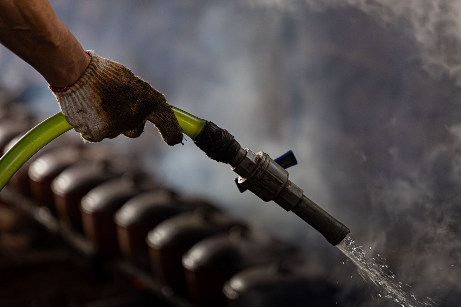 Hand mit Handschuh am Industrieschlauch, Dampf im Hintergrund